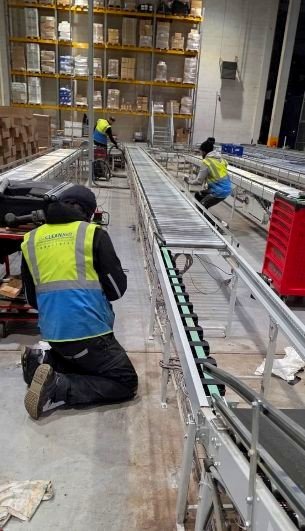 CleanBelt technicians performing maintenance on automated roller conveyor systems in a warehouse logistics center.