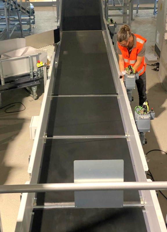 CleanBelt technician in PPE performing maintenance on a clean industrial incline conveyor belt system.