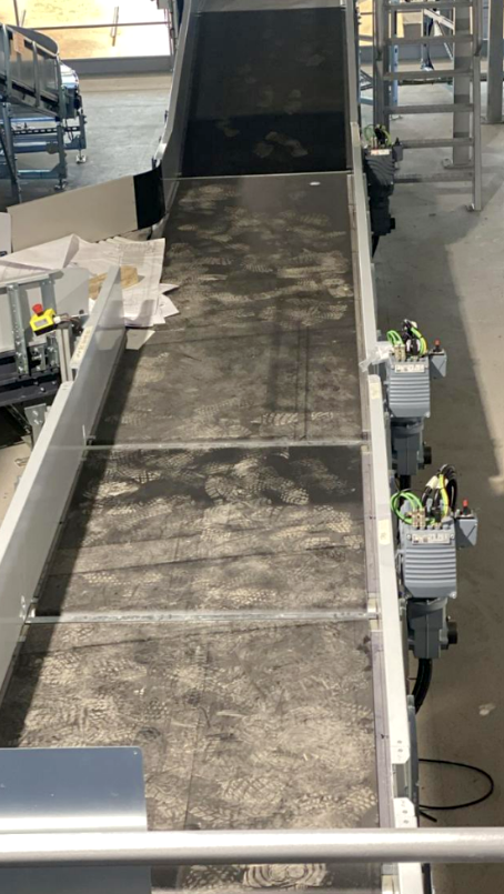 A heavily contaminated industrial conveyor belt visibly covered in dust and footprints, posing slippage and tracking risks.
