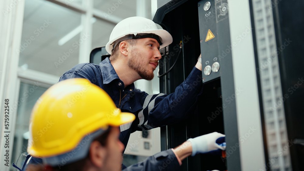 CleanBelt maintenance team in safety wear are assisting in adjusting and maintaining CNC machine in the factory. Male factory workers are examining the industrial machine to find an error.